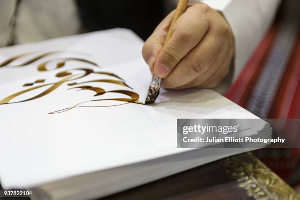 a man writes out traditional arabic script. - arabic script stock-fotos und bilder