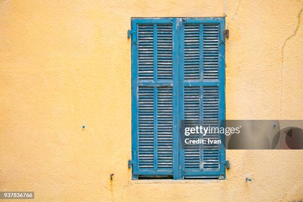 yellow wall with blue window - fensterladen stock-fotos und bilder