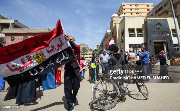 An Egyptian man walks carrying a national flag defaced with a caption in Arabic reading on each coloured stripe "the colour of our blood [red], the...