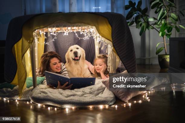 happy mother and daughter relaxing with a dog in a tent and reading a book. - animal related occupation stock pictures, royalty-free photos & images