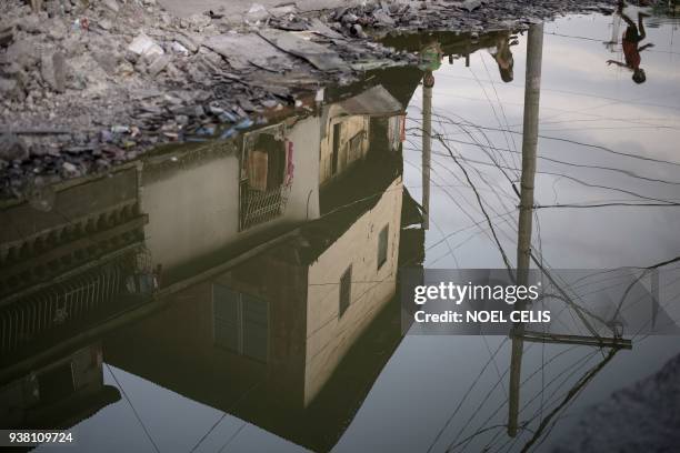 Child is reflected in a puddle on a street in Manila on March 26, 2018.