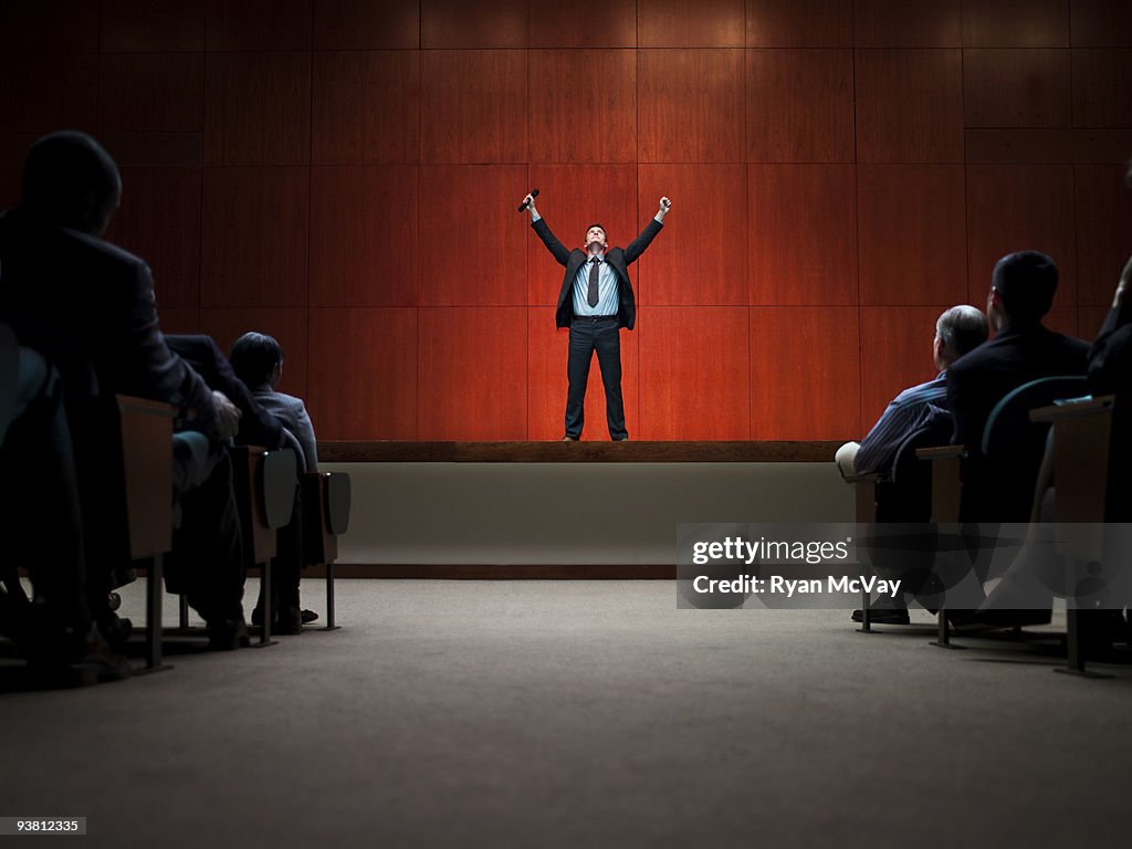 Business man on stage with arms raised 