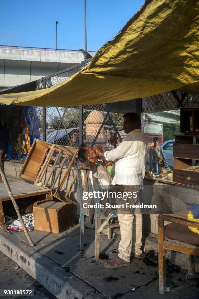 Roadside barber shaves a man at a stall near Nizamuddin East market, New Delhi, India.