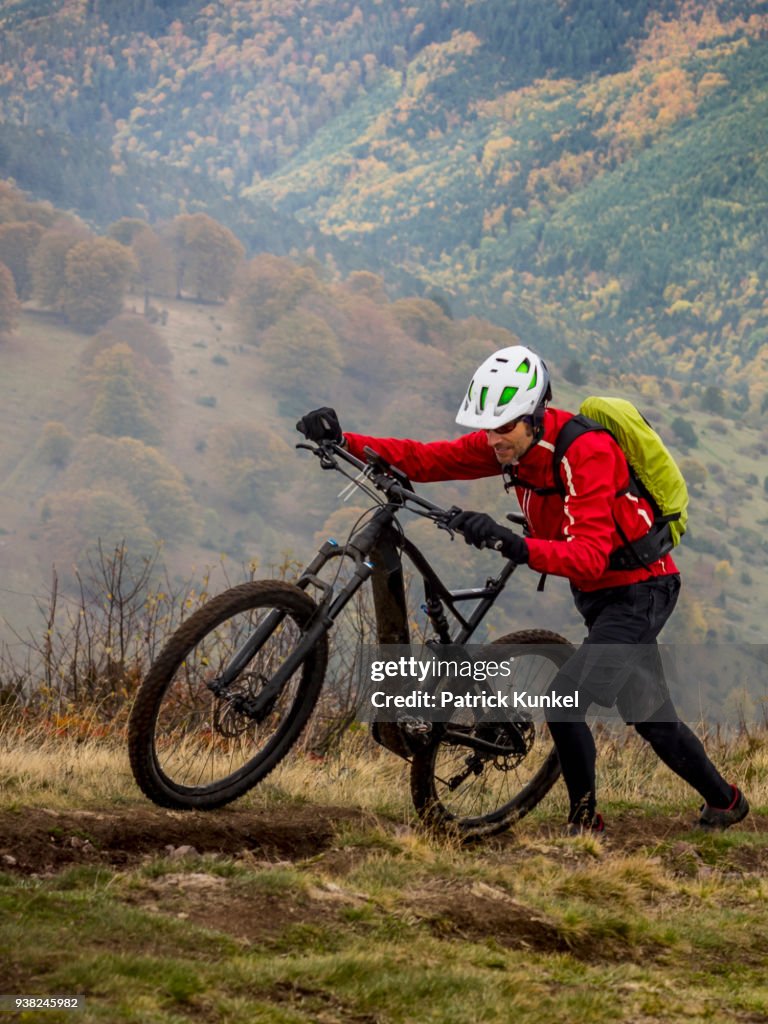 Man walking electric mountain bike on cycling tour, Vosges, France