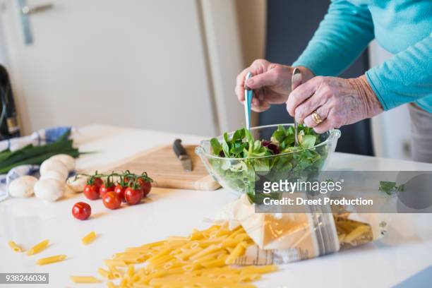 old woman mixing salad on the kitchen table - menschliches körperteil stock pictures, royalty-free photos & images