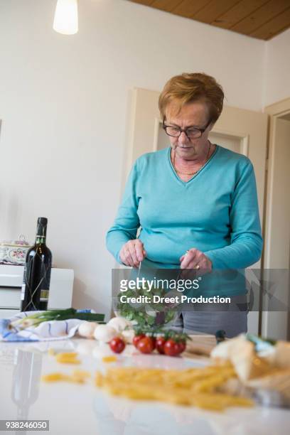 old woman mixing salad on the kitchen table - vertikal - fotografias e filmes do acervo