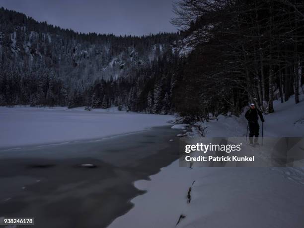 man hiking with snowshoes on the shore of lake feldsee, black forest, baden-württemberg, germany - scheinwerfer stockfoto's en -beelden