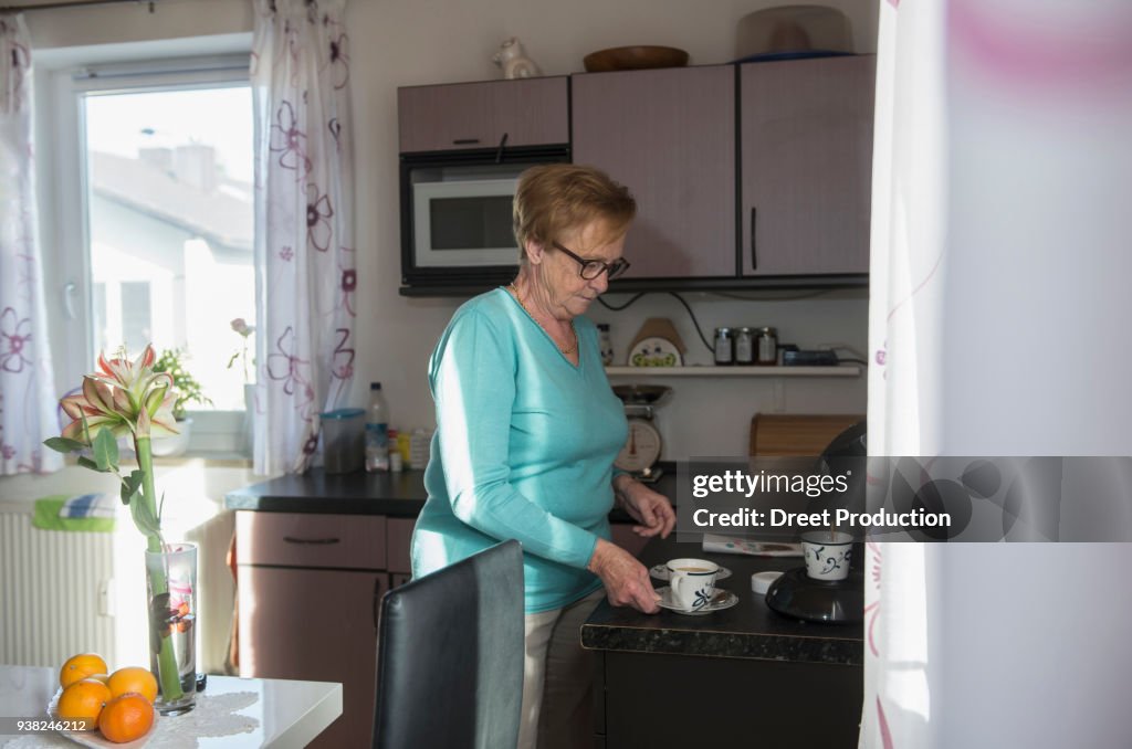 Senior woman taking cup of coffee from kitchen counter