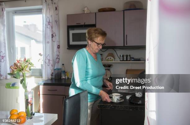 senior woman taking cup of coffee from kitchen counter - trinken flasche foto e immagini stock