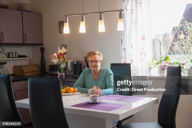 senior woman drinking coffee at home - brille frau stockfoto's en -beelden