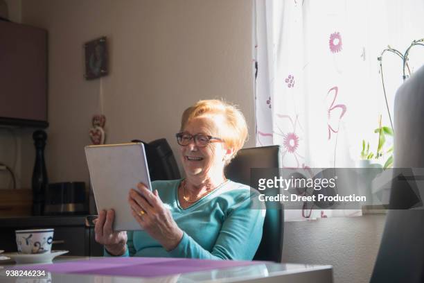 happy old woman watching digital tablet at dining table - freizeitaktivität imagens e fotografias de stock