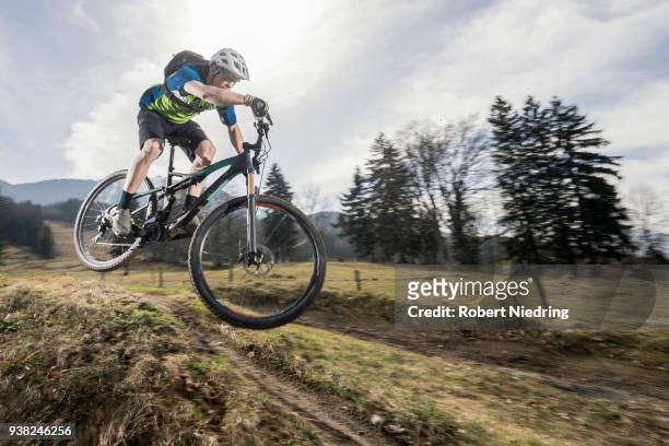 mountain biker performing jump on bicycle on single track, bavaria, germany - ganzkörperansicht photos et images de collection