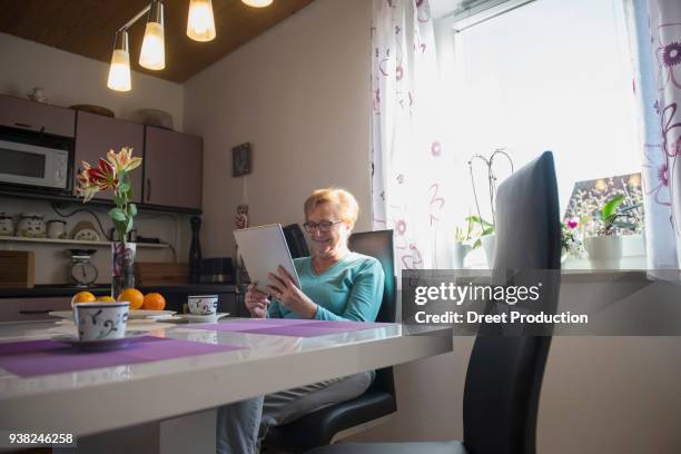 happy old woman watching digital tablet at breakfast table - vergnügen stockfoto's en -beelden