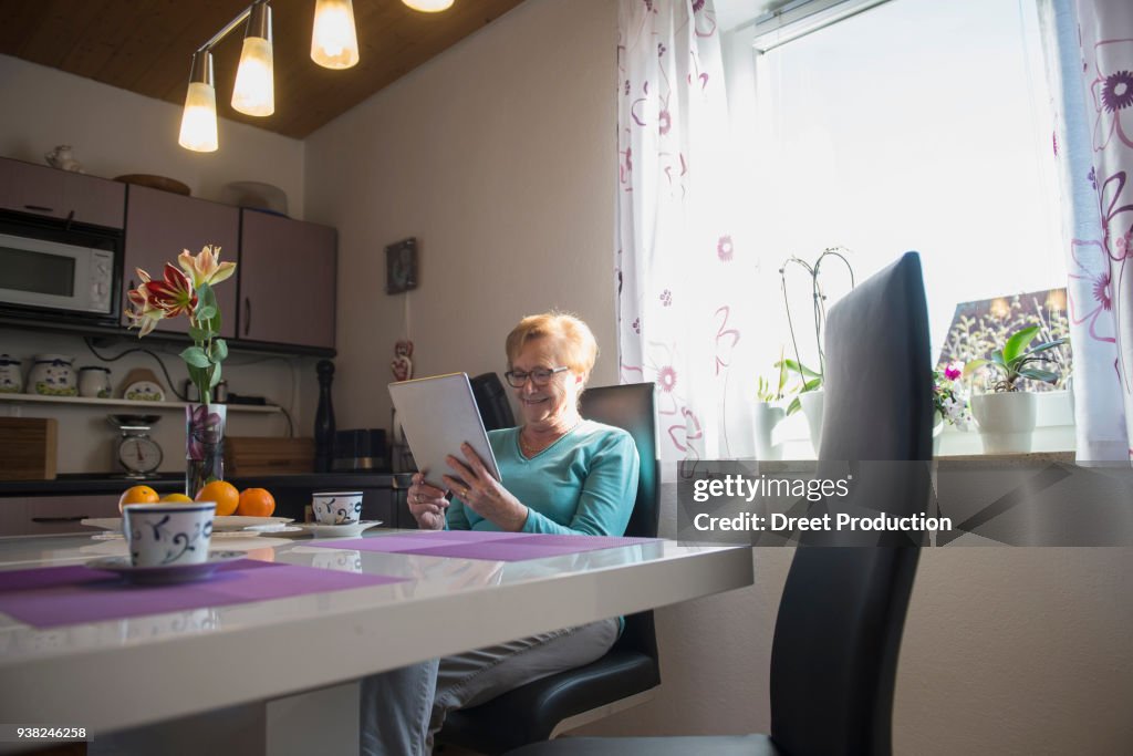 Happy old woman watching digital tablet at breakfast table