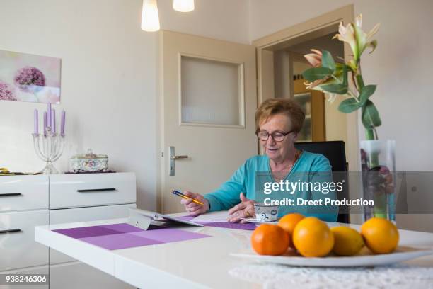 old woman writing in book at dining table - eine frau allein ストックフォトと画像