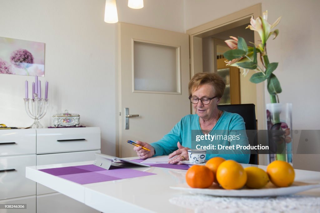 Old woman writing in book at dining table