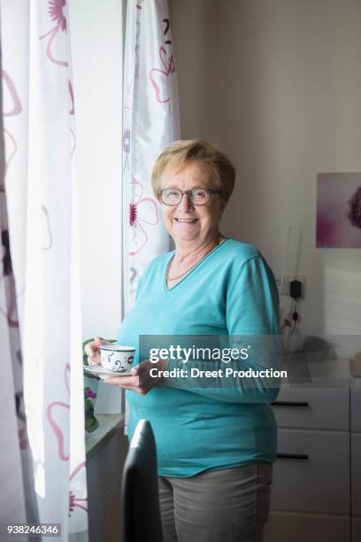 smiling old woman at the window with a cup of coffee - eine frau allein ストックフォトと画像