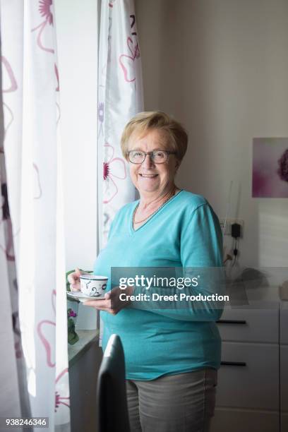 smiling old woman at the window with a cup of coffee - vertikal - fotografias e filmes do acervo