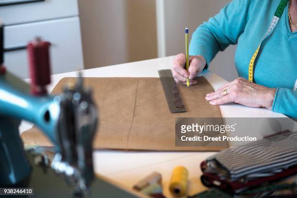 old woman drawing pattern on sewing desk - menschliches körperteil foto e immagini stock