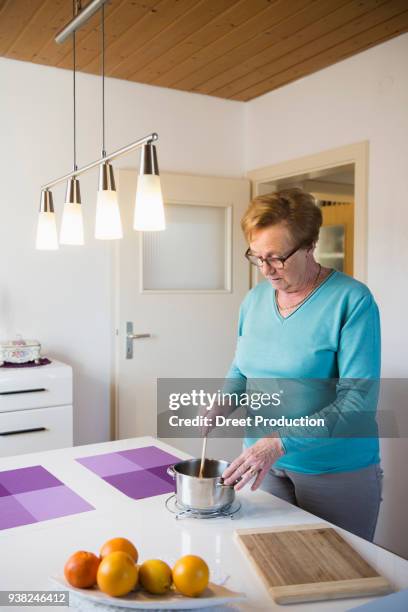 old woman stirring in a pot at dining table - brille frau stockfoto's en -beelden