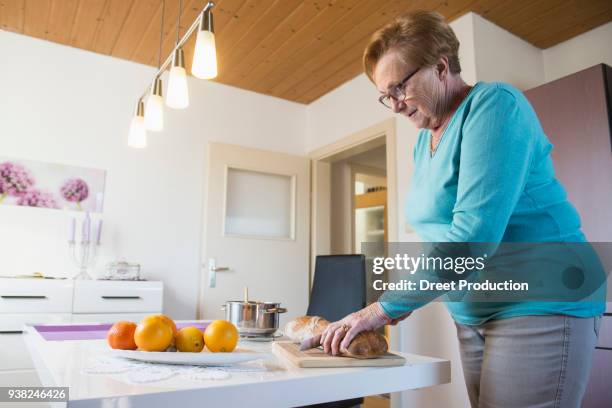 old woman cutting bread on breakfast table - küchenmesser foto e immagini stock