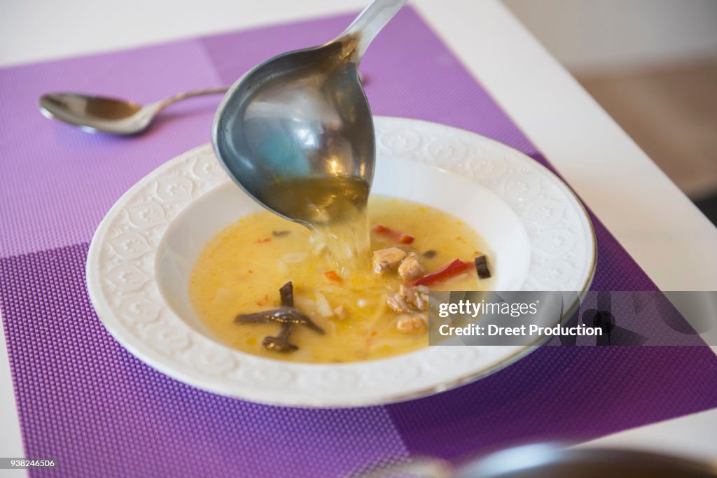Noodle soup being poured in a soup plate on dining table