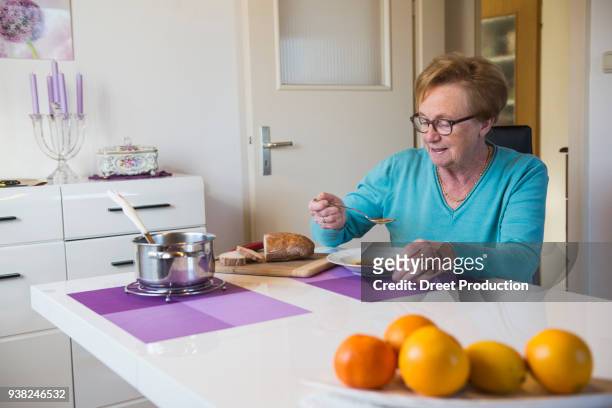 old woman eating soup at dining table - tür stockfoto's en -beelden