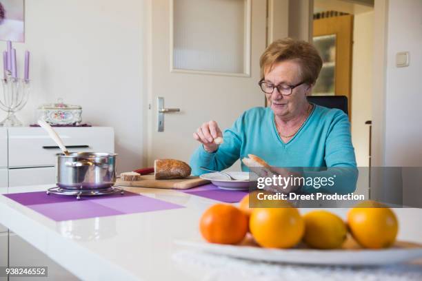old woman eating bread at lunch table - pfanne stockfoto's en -beelden