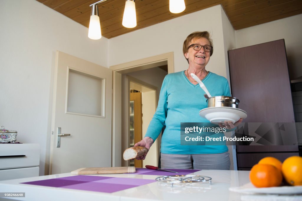 Happy old woman with pot, bread and soup plates in her hands