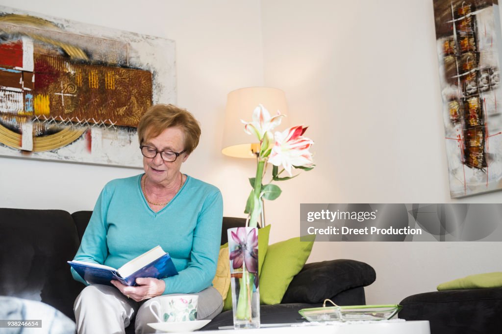 Old woman sitting on sofa reading a book