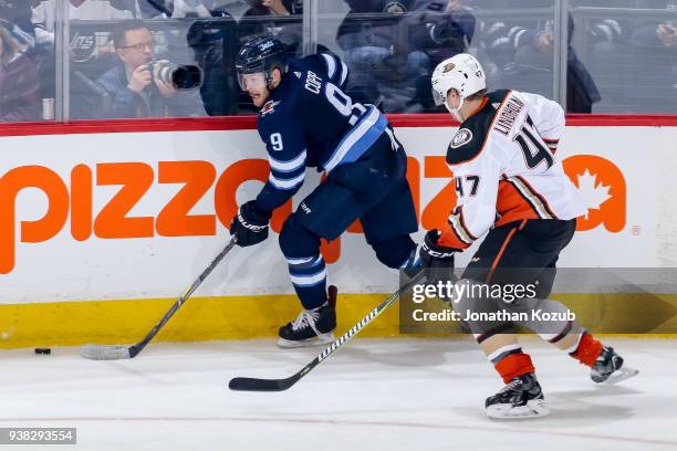 Andrew Copp of the Winnipeg Jets plays the puck along the boards as Hampus Lindholm of the Anaheim Ducks gives chase during second period action at...