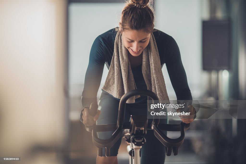 Feliz mujer atleta ciclismo en bicicleta estática en un gimnasio.