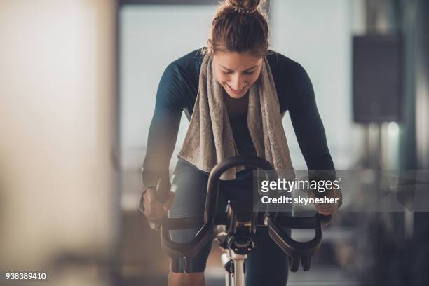 feliz mujer atleta ciclismo en bicicleta estática en un gimnasio. - exercise bike fotografías e imágenes de stock
