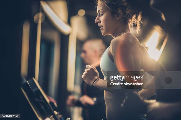 athletic woman running on treadmills during sports training in a health club. - treadmill stock pictures, royalty-free photos & images
