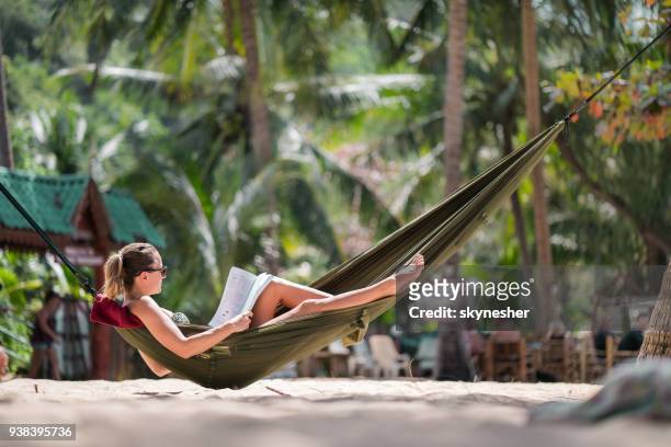 relaxed woman sunbathing in hammock on the beach and reading a book. - woman on beach reading stock pictures, royalty-free photos & images