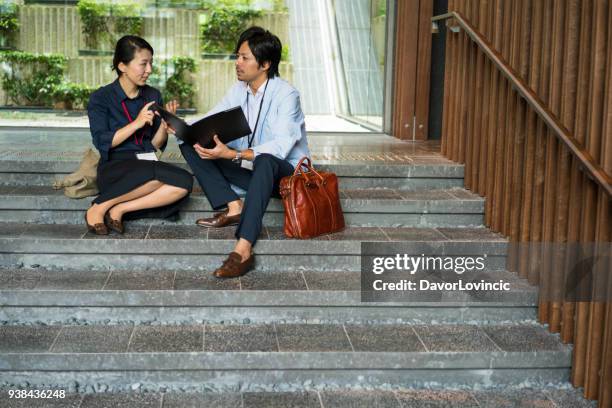 middelbare leeftijd zakenvrouw bespreken met zakenman, zittend op trappen in gebouw de hal, kyoto, japan. - lypsekyo16 stockfoto's en -beelden