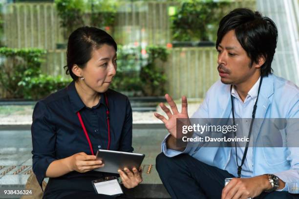 middelbare leeftijd zakenvrouw bespreken met zakenman, zittend op trappen in gebouw de hal, kyoto, japan. - lypsekyo16 stockfoto's en -beelden