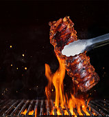 Pork ribs over flaming grill grid, isolated on black background.