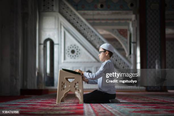 muslim boy reading the holy koran in mosque - koran stock pictures, royalty-free photos & images