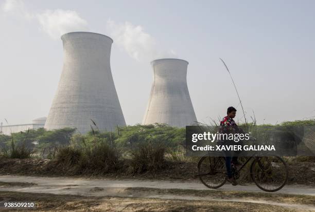 An Indian man cycles along a dirt road next to the Norora Atomic Power Station near Norora in Uttar Pradesh state on March 27, 2018. / AFP PHOTO /...