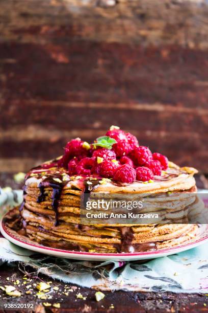 stack of wheat golden pancakes or pancake cake with freshly picked raspberry, chopped pistachios, chocolate sauce on a dessert plate, selective focus - freshers week stock pictures, royalty-free photos & images