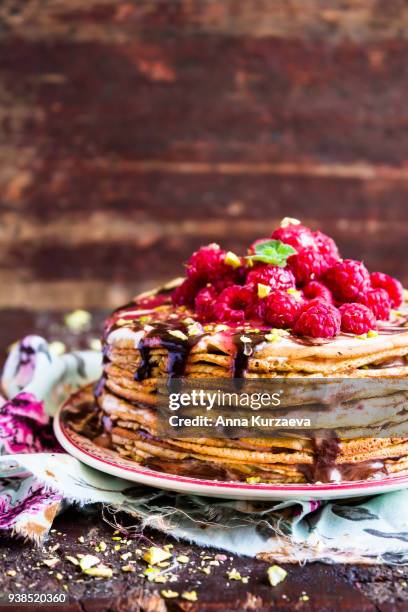 stack of wheat golden pancakes or pancake cake with freshly picked raspberry, chopped pistachios, chocolate sauce on a dessert plate, selective focus - raspberry sauce stock pictures, royalty-free photos & images