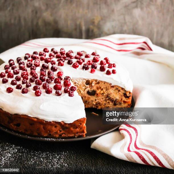 homemade christmas cake with dried fruits decorated with sweet vanilla meringue, fresh cranberry and icing sugar on a plate, selective focus. easter cake. - christmas cake stock pictures, royalty-free photos & images