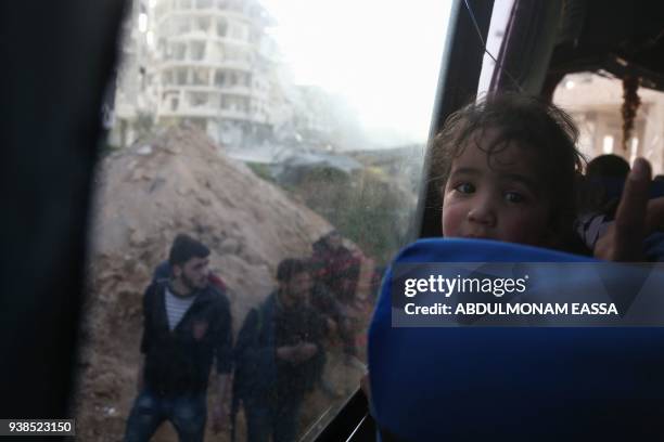 Convoy transporting Syrian civilians and rebel fighters drives past destroyed buildings in Arbin in Eastern Ghouta as they are evacuated from the...