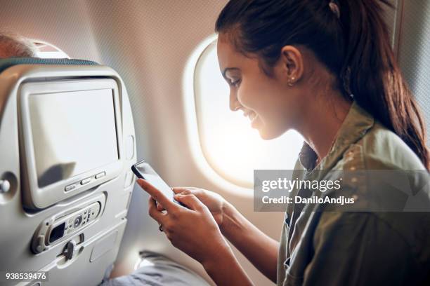 beautiful young woman using her smartphone in the plane - mobile on plane stock pictures, royalty-free photos & images