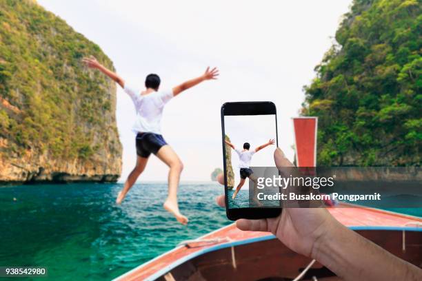 smartphone photographing asian young man jumping from boat into the andaman sea, thailand - image focus technique photos stock pictures, royalty-free photos & images