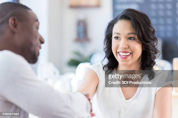 young woman shakes hands with unrecognizable man in coffee shop - blind date stock pictures, royalty-free photos & images