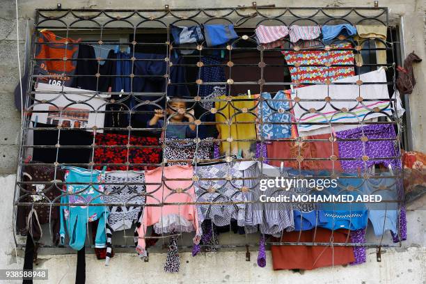 Palestinian child stands behind hanging laundry on the window of his family's home in Beit Hanun in the northern of Gaza Strip on March 27, 2018.