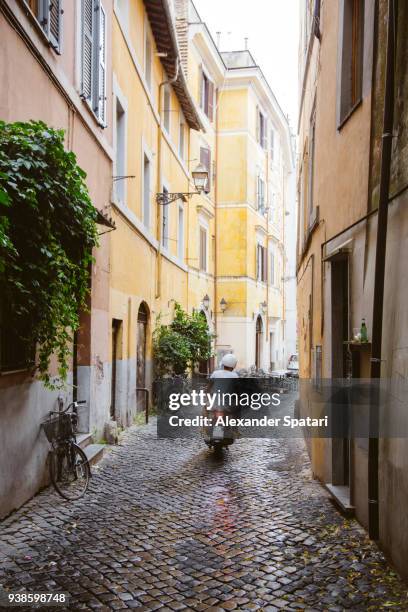 young man riding a scooter in narrow cobbled street in trastevere rome - holiday scooter fotografías e imágenes de stock
