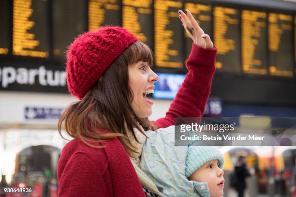 mother with child in baby carrier is greeting by waving hand in arrival hall. - waving hands goodbye photos et images de collection